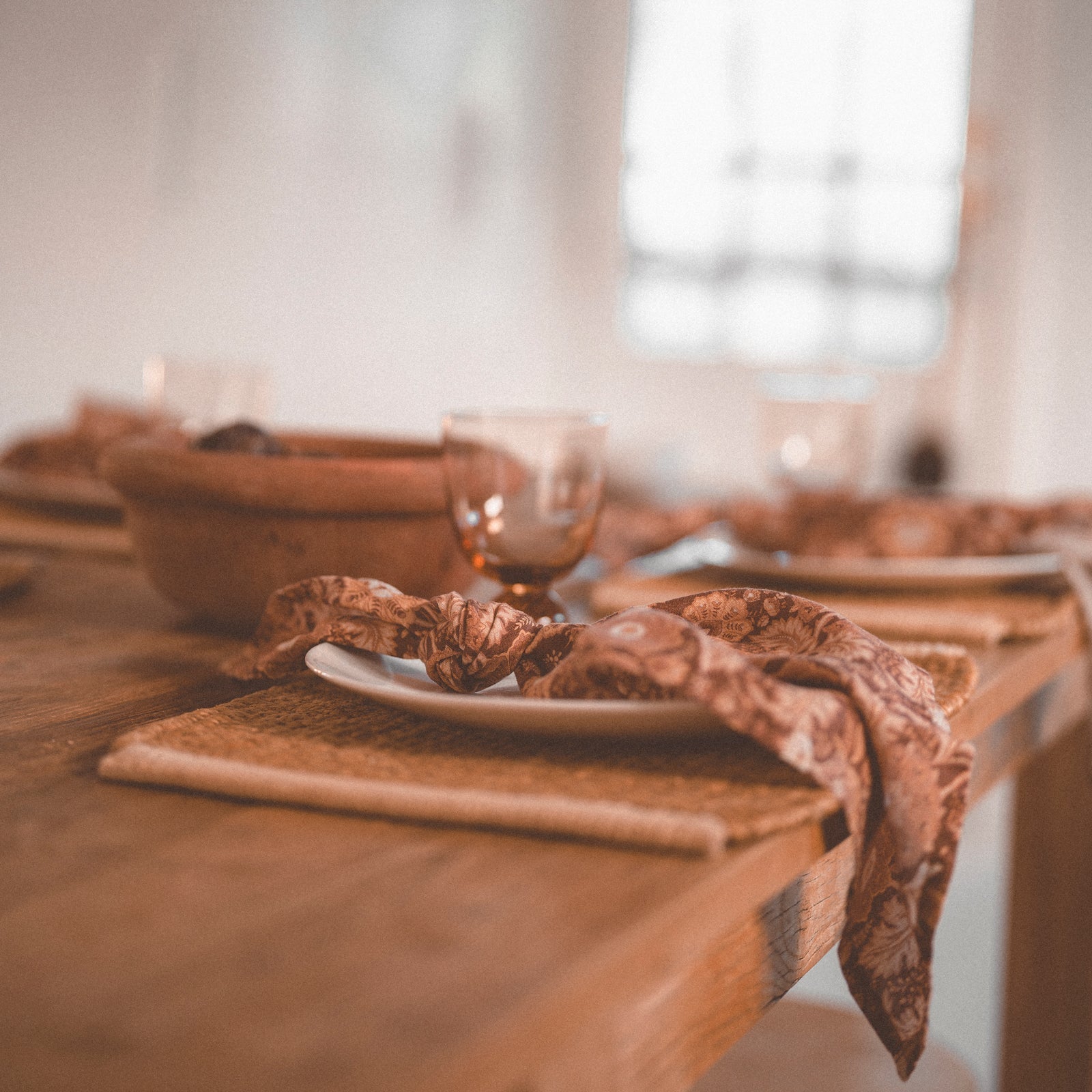 Paisley printed linen napkin in earthy colours sits on a table top tied casually in a knot