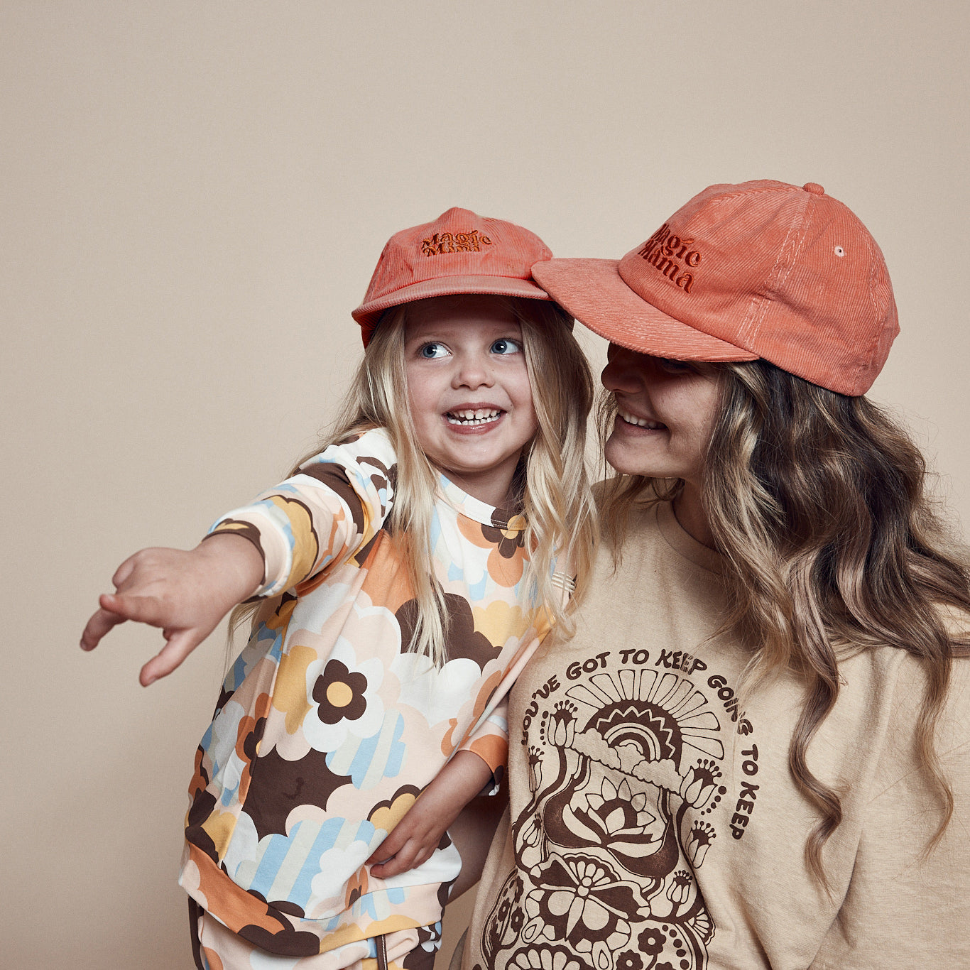 Mother and daughter wearing coordinating  Magic Mini Corduroy cap and Magic Mama corduroy cap. Both are pink with embroidery on center front in darker tone of pink.