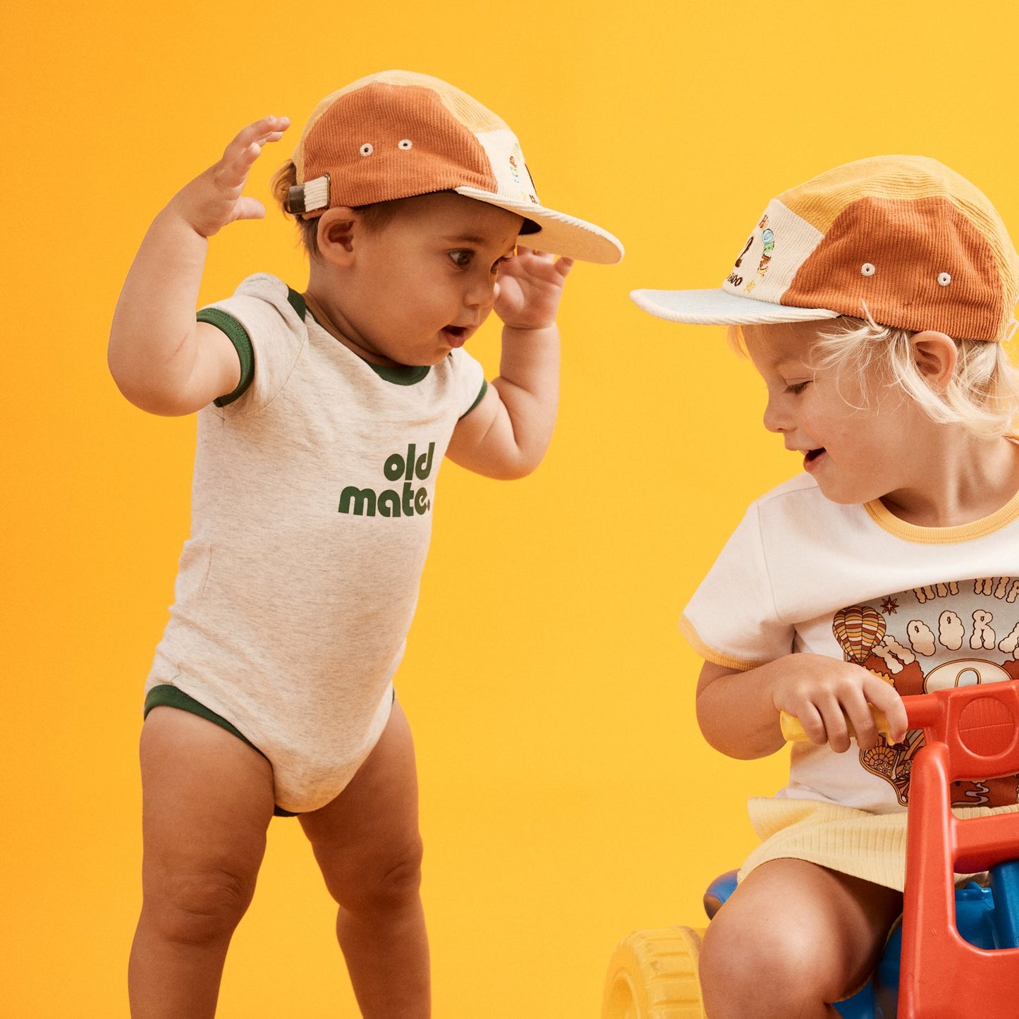 Image of happy one year old  standing up wearing a cap and natural grey marled  onesie  with contrast green ringer bind at sleeve, neckline and hemp. Old Mate in green printed at center front.
