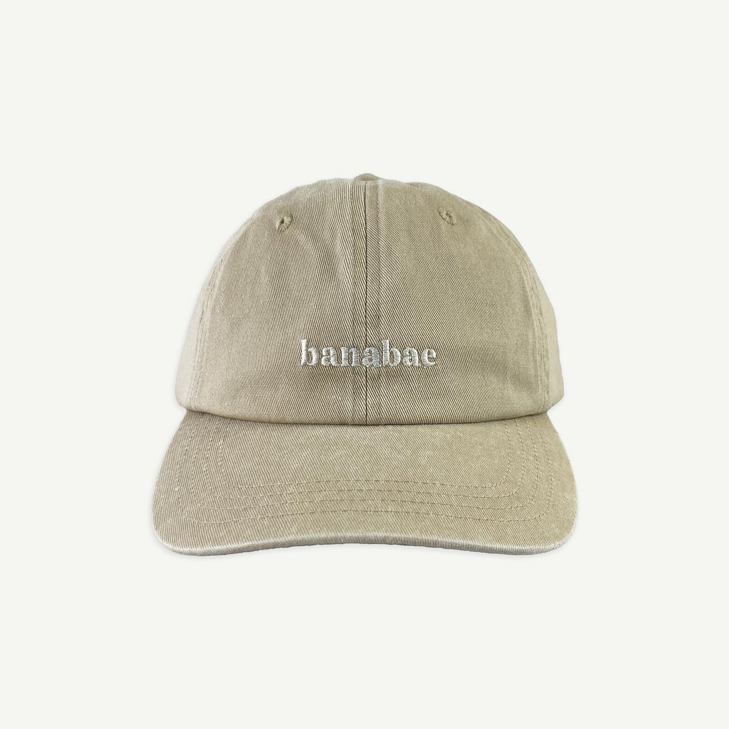 Front view of Banabae washed sand cap in organic cotton twill, Banabae embroidery at the center front in contrast white.  