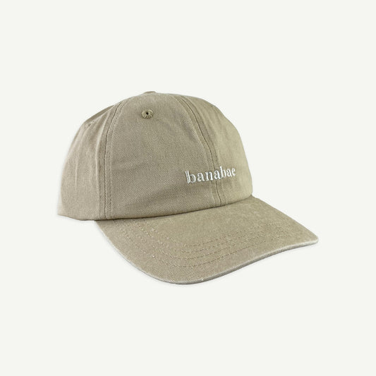 Side view of Banabae washed sand cap in organic cotton twill, Banabae embroidery at the center front in contrast white.